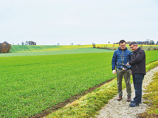 Zwei Männer stehen auf einem Feldweg und zeigen sich etwas in einem Tablet.